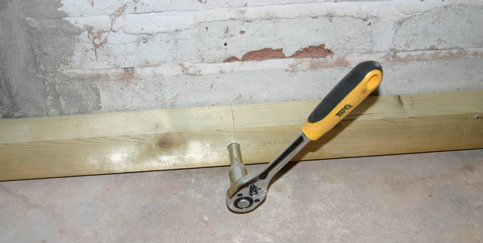 Using a ratchet spanner to screw stud to the garage wall.