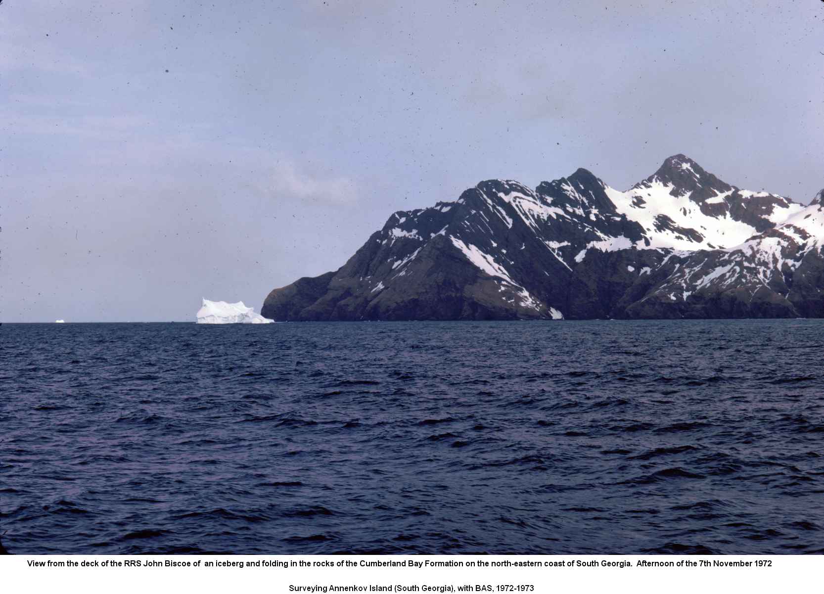View from the deck of the RRS John Biscoe of  an iceberg and folding in the rocks of the Cumberland Bay Formation on the north-eastern coast of South Georgia.  Afternoon of the 7th November 1972.