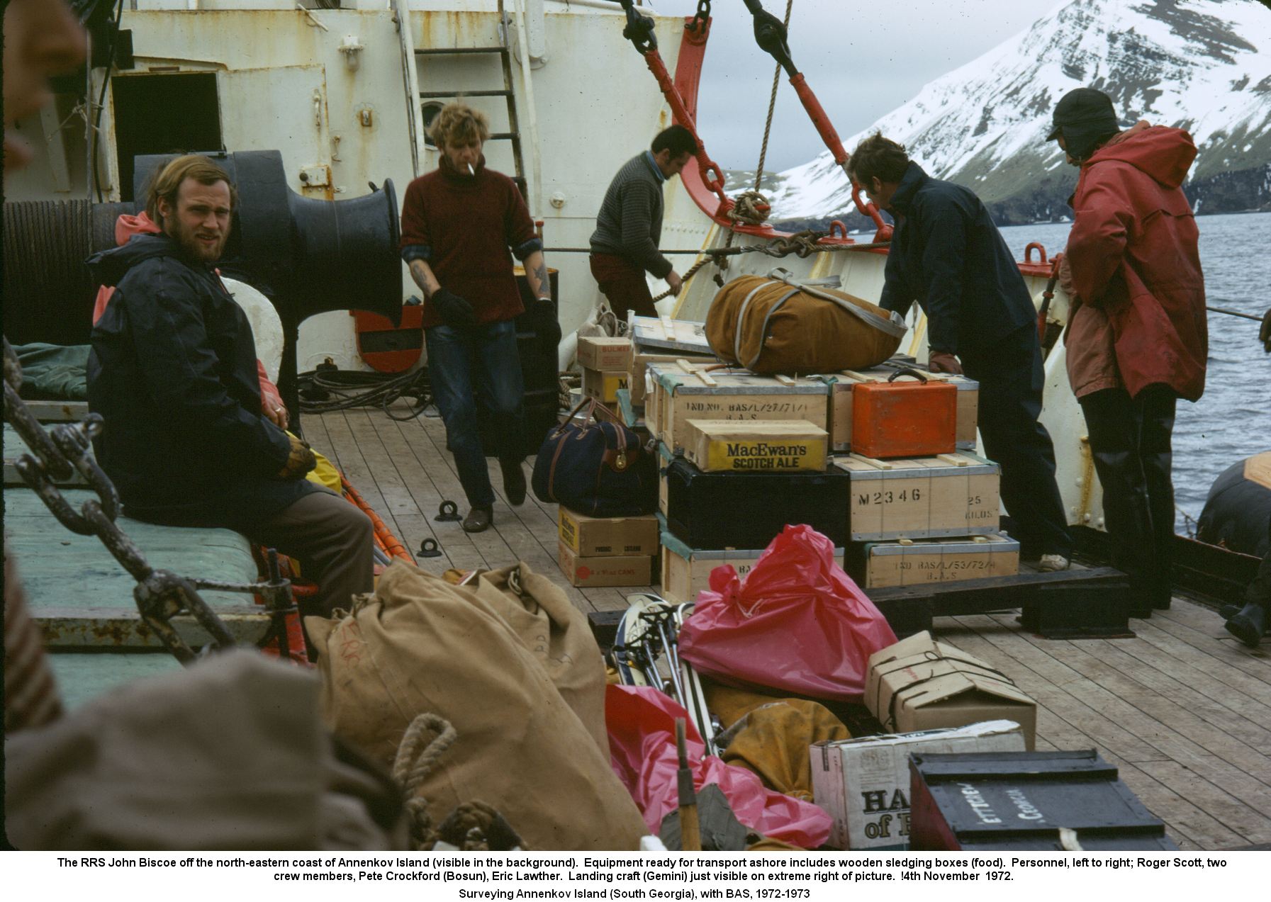 The RRS John Biscoe off the north-eastern coast of Annenkov Island (visible in the background).  Equipment ready for transport ashore includes wooden sledging boxes (food).  Personnel, left to right; Roger Scott, two 
crew members, Pete Crockford (Bosun), Eric Lawther.  Landing craft (Gemini) just visible on extreme right of picture.  !4th November  1972.
